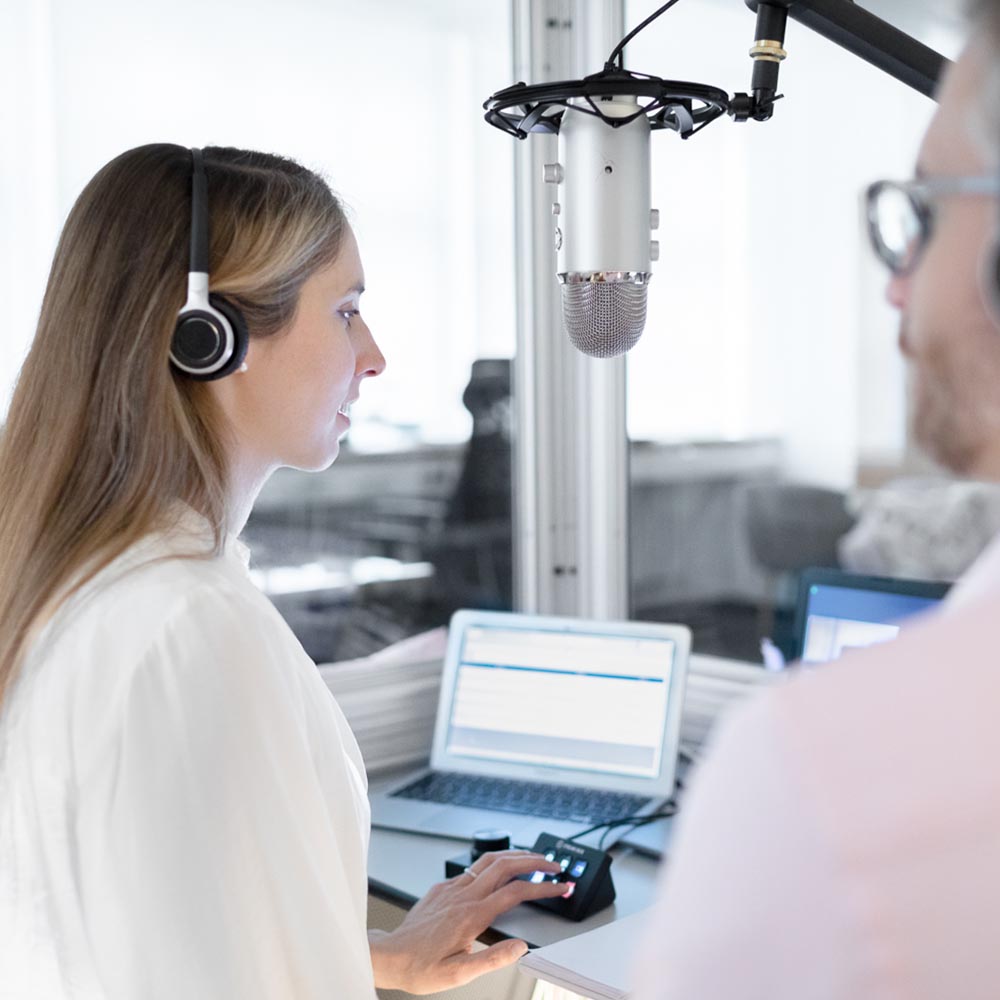 Mannheimer Dolmetschstudio: Eine Konferenzdolmetscherin sitzt in der Kabine mit Kopfhörer und spricht in ein Studiomikrofon. Mit der linken Hand bedient sie die Konsole.